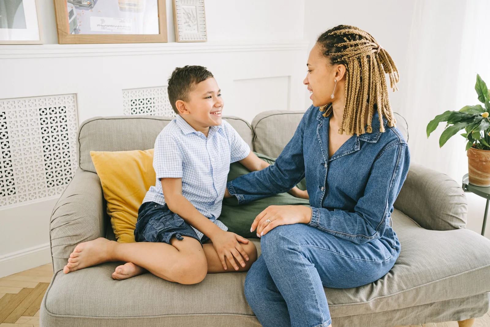 A parent and her son sitting together on a sofa at home, turned toward each other and smiling mid-conversation.